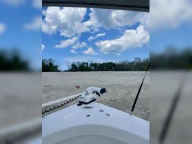 A close-up view of a boat's bow with a motor, set against a backdrop of a sandy shore and blue sky — perfect for showcasing boat features and design.