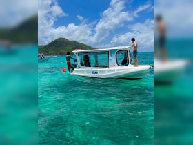 A lively scene featuring guests enjoying water activities around a boat in crystal-clear waters, perfect for snorkeling and fun in the sun.