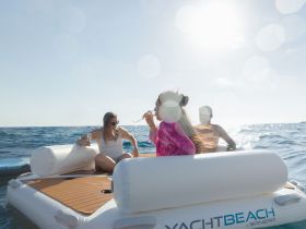 A group of friends enjoys cocktails on a floating mat in the ocean, capturing the essence of a fun day on the water.