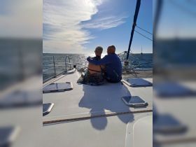 A couple enjoys a romantic moment on the deck of a sailboat, gazing at the sunset over the water — an idyllic setting for love and connection.
