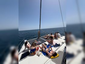 A lively group enjoys sunbathing on the deck of a catamaran, perfect for summer parties and relaxation on the water.