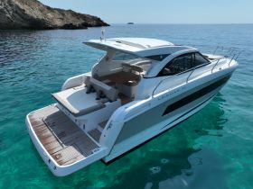 A stunning aerial view of a sleek yacht, the Leader 36, gliding through crystal-clear waters, showcasing its elegant design and spacious deck.