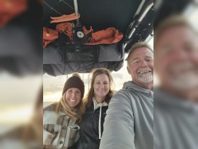 A cheerful group of friends takes a selfie aboard a boat, capturing a memorable moment against a beautiful sunset backdrop.