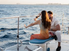 A couple enjoys a romantic moment on the deck of a yacht, gazing at the sunset over the water — perfect for intimate getaways or special celebrations.