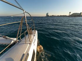 A side view of a catamaran cruising through calm waters, showcasing the vessel's sleek design against a backdrop of a coastal skyline.