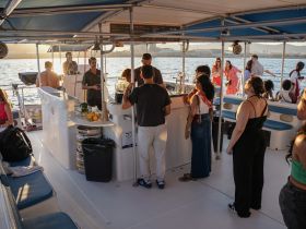 A lively group enjoys drinks and socializing aboard a boat during a sunset cruise, creating a perfect atmosphere for celebrations and gatherings on the water.