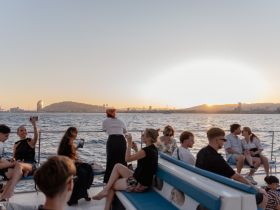 A lively group enjoys a sunset cruise on a yacht, capturing memories with drinks and laughter against the stunning backdrop of the Barcelona skyline.