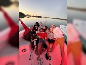 A lively group enjoys a fun evening on a boat, celebrating together as the sun sets over the water — perfect for unforgettable gatherings and parties.