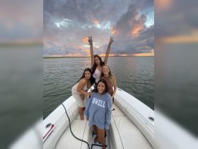 A group of friends celebrates on a boat at sunset, capturing joyful moments against a stunning sky — perfect for memorable outings and gatherings on the water.