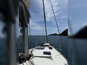 A serene view from the deck of a sailboat, showcasing the vessel's sleek lines against a backdrop of calm waters and distant land — perfect for sailing enthusiasts.