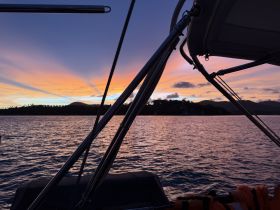 A serene sunset view from the deck of a boat, showcasing vibrant colors over the water and distant hills — perfect for capturing the tranquility of evening cruises.