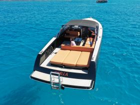 A stylish boat with comfortable seating is captured in vibrant turquoise waters, showcasing a group enjoying their time on the water.
