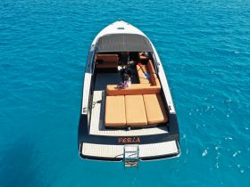 Aerial view of the 'Perla' speedboat anchored in vibrant turquoise waters, featuring spacious seating and a relaxing atmosphere perfect for day trips.