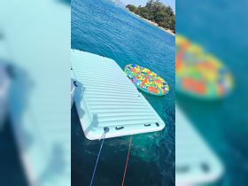 A vibrant inflatable floating mat and a colorful tube are anchored in crystal-clear waters, perfect for fun and relaxation during a day on the boat.