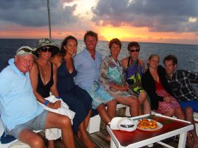A cheerful group enjoys a sunset cruise on a boat, capturing a moment of celebration with drinks and stunning ocean views.