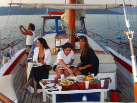 A lively group enjoys a meal on deck while sailing, capturing the essence of a perfect day on the water with good food and great company.