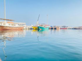 A serene view of various boats docked in a harbor, reflecting beautifully on the calm waters under a clear blue sky.