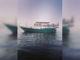 A vibrant boat filled with guests glides through calm waters, showcasing a perfect day for a scenic tour or cruise adventure.