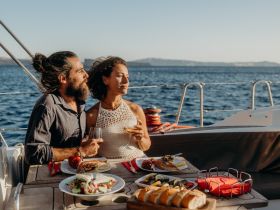 A couple enjoys a romantic dining experience on a yacht, complete with delicious food and cocktails, set against a stunning ocean backdrop.
