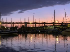 A serene sunset view over a marina, showcasing boats and their reflections in the calm water — a picturesque moment perfect for evening strolls by the harbor.