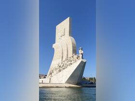 A striking monument featuring intricate sculptures, set against a clear blue sky, with people visible nearby, showcasing a blend of art and history.