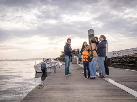 A group of people gathers on the dock, discussing plans near a boat, creating a lively atmosphere perfect for pre-trip excitement.