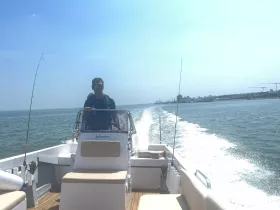 A man confidently navigates a fishing boat on the water, showcasing the thrill of a day out at sea.
