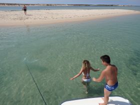 Two children enjoy a playful moment wading into the clear waters near a sandy beach, capturing the essence of summer fun and adventure.