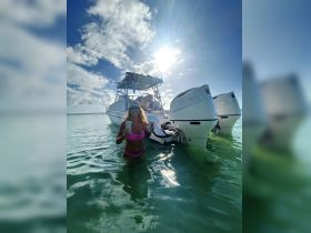 A woman enjoys a refreshing drink while wading in the shallow waters next to a boat, capturing the essence of a fun day on the water.