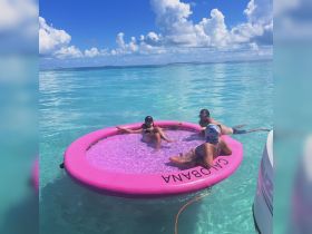 A fun group enjoys a floating mat in crystal-clear waters, perfect for relaxation and sunbathing during a tropical getaway.