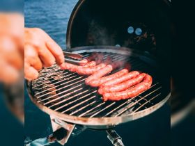 A hand skillfully flips sausages on a grill aboard a boat, showcasing the perfect setup for a delicious barbecue experience on the water.