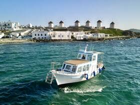 A charming boat navigates the turquoise waters near iconic windmills and whitewashed buildings, showcasing the beauty of coastal scenery.