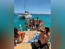 A lively group enjoys a sunny day aboard a catamaran, celebrating with drinks and laughter in the beautiful turquoise waters.