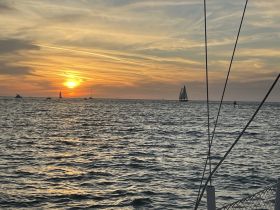 A stunning sunset over the ocean with sailboats in the distance, capturing the serene beauty of a sailing experience.