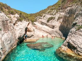 A group enjoys a refreshing swim in crystal-clear waters surrounded by stunning rocky cliffs — a perfect spot for adventure and relaxation.