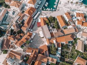 An aerial view of a coastal town featuring red-roofed buildings and a marina, showcasing the charming architecture and layout of the area.