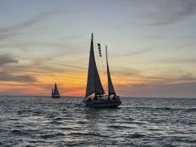Sailboats glide across the ocean at sunset, creating a picturesque scene perfect for romantic evenings or sailing adventures.