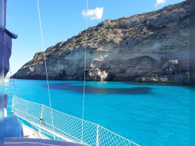A stunning view of turquoise waters and rocky coastline from a sailboat, showcasing the beauty of a sailing adventure in picturesque surroundings.