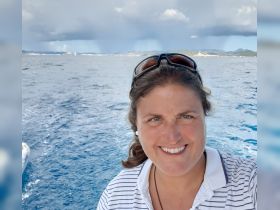 A woman smiles for a selfie on a boat, with a scenic backdrop of water and distant land — capturing the joy of a boating adventure.