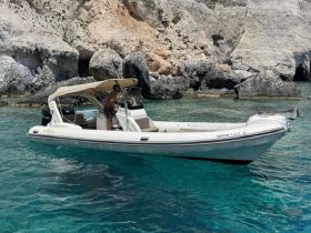 A person stands on a sleek boat navigating through crystal-clear waters, surrounded by stunning rocky cliffs — a perfect scene for adventure seekers exploring coastal beauty.