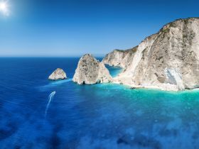 A stunning aerial view of rocky cliffs and turquoise waters, showcasing the breathtaking coastline — perfect for exploring hidden gems by boat.