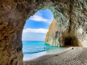 A stunning view from inside a cave looking out to a beautiful beach and turquoise waters, with a person enjoying the serene environment — a perfect spot for relaxation and exploration.