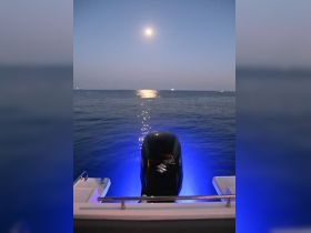 A serene night view of a boat's motor illuminated by blue lights, with the moon reflecting on the calm ocean waters — perfect for nighttime boating adventures.