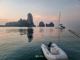A serene view of a catamaran anchored in calm waters, surrounded by stunning rock formations at sunset — perfect for tranquil sailing experiences.