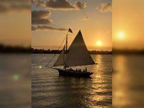 A beautiful sunset view featuring a sailboat with guests enjoying the serene waters — perfect for romantic evenings or group celebrations on the water.