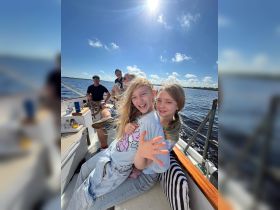 Two joyful children pose for a photo while sailing, capturing a fun moment on the water with family and friends.