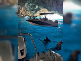 A lively scene inside a stunning cave with people swimming in vibrant blue waters while boats are anchored nearby, perfect for adventurous outings and exploring natural wonders.