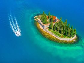 A stunning aerial view of a boat cruising past a picturesque island surrounded by vibrant turquoise waters, showcasing the beauty of coastal destinations.