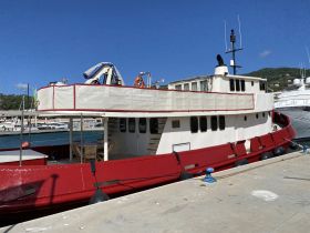 A striking red and white boat docked at the marina, showcasing its unique design and structure against a clear blue sky.
