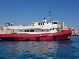A striking red boat docked against a clear blue sky, showcasing its unique hull design and structure, perfect for maritime enthusiasts.